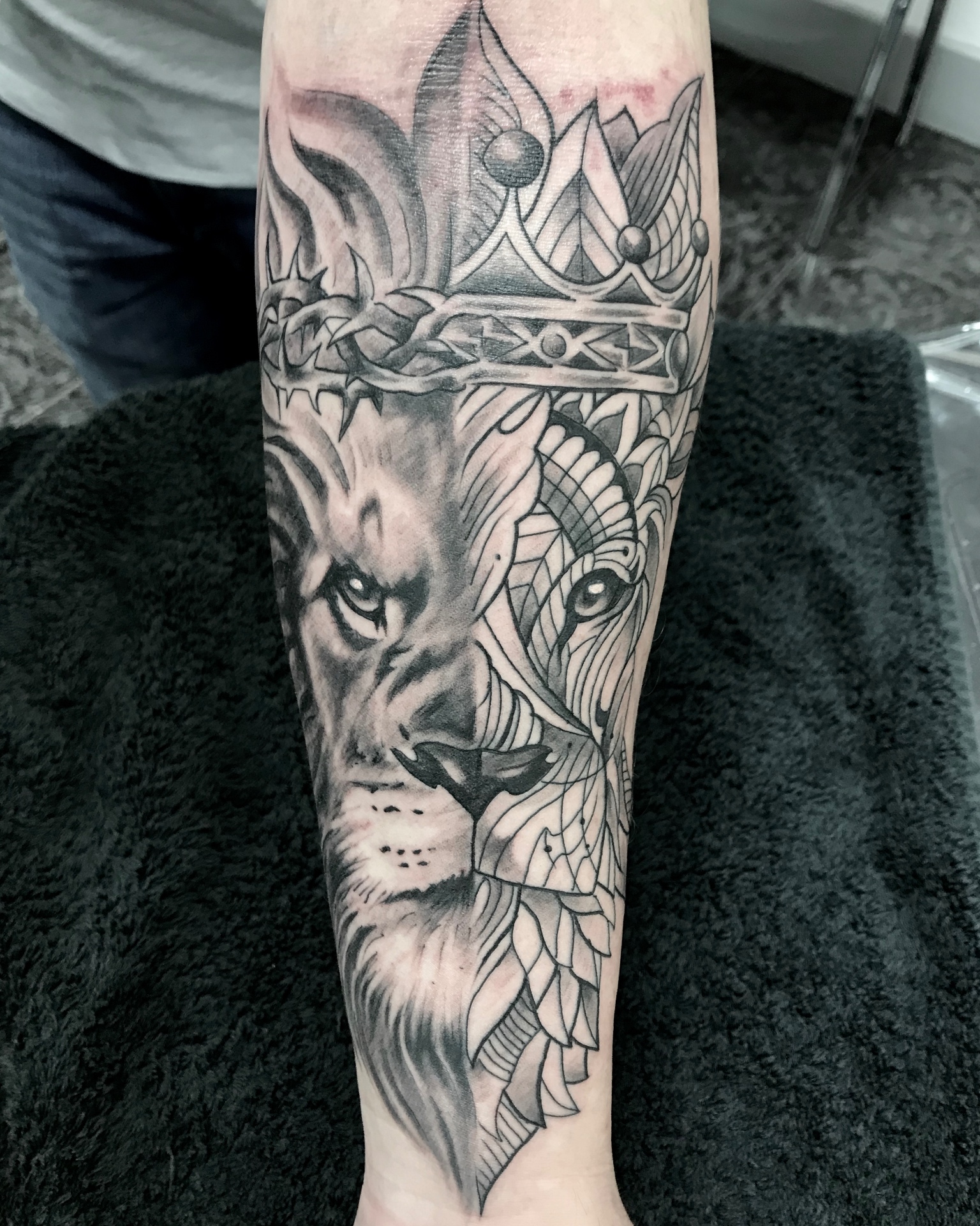Black and grey lion with crown of thorns and ornamental forearm tattoo by Steve Evans