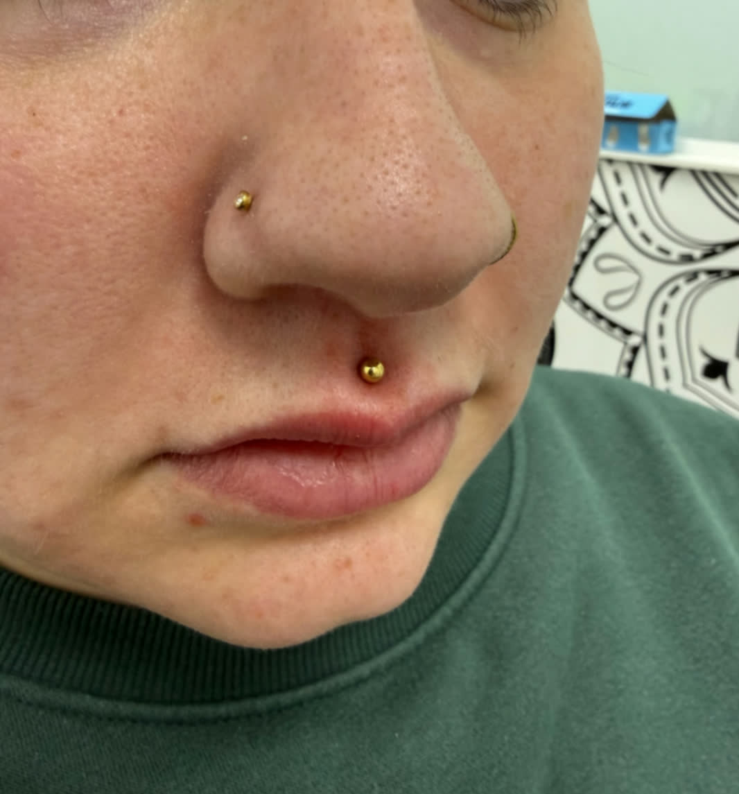 Gold nostril and philtrum piercings with clean, minimal jewellery placement