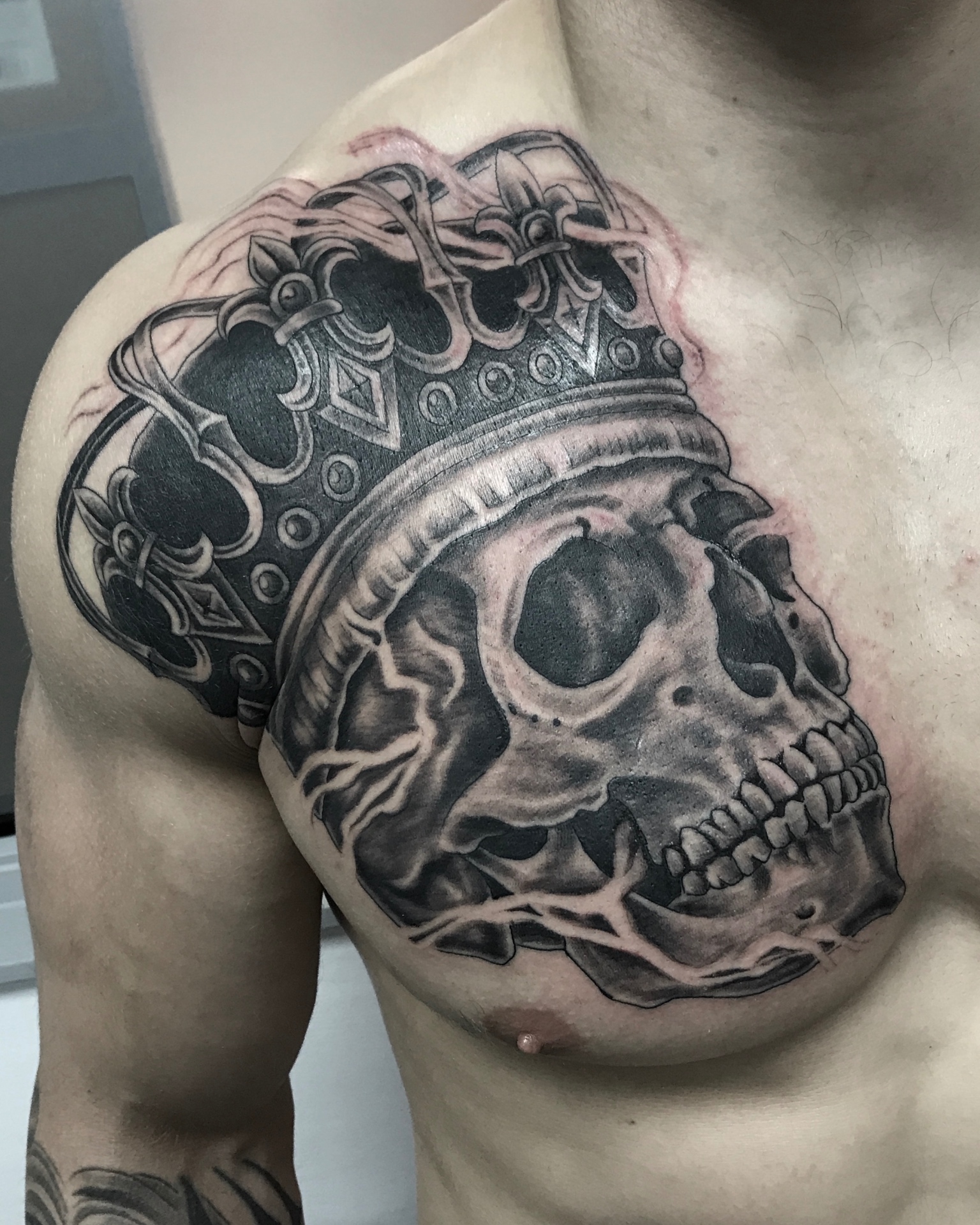 Black and grey crowned skull chest and shoulder tattoo by Steve Evans